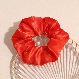 Primo piano di un elastico per capelli in raso rosso lucido su un vassoio di vetro