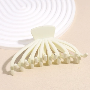 Close-up of a matte cream octopus hair claw clip on a minimalist white textured tray
