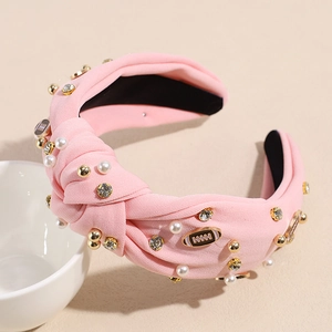 Detail eines rosa geknoteten Haarreifens mit weißen Perlen, Strass und Rugby-Anhänger