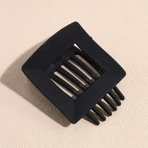 Close-up of a matte black hollow square hair claw clip on a light beige stone base