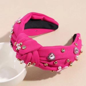 Detail eines fuchsiafarbenen Knotenstirnbands mit weißen Perlen und rosa Strasssteinen
