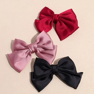 Trois barrettes à nœuds élégantes en satin rouge, rose et noir sur un fond beige délicat