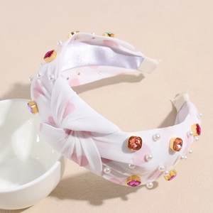 Close-up of white knotted headband with pink hearts, pearls and colorful rhinestones