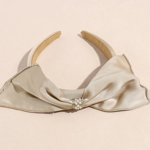 Détail du serre-tête en satin champagne avec bords en strass et centre en perles