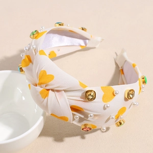 Detail of a white knotted headband with heart prints, pearls and colored rhinestones