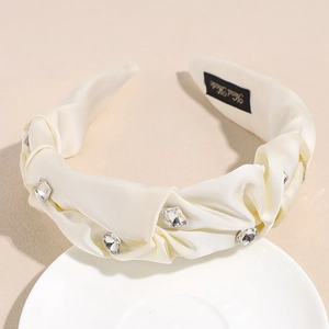 Detail eines cremefarbenen Satin-Haarreifs mit Knoten, Strasssteinen und Handarbeits-Label