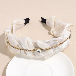 Detail eines eleganten weißen Haarreifens aus Satin mit Goldkette und Kristallen auf Teller
