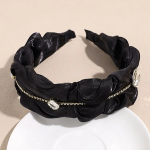 Detail eines luxuriösen Plissee-Stirnbands mit funkelnden Kristallen auf schwarzem Satin