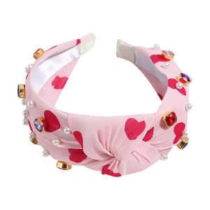Pink knotted headband with heart patterns, pearls and colorful rhinestones on white background