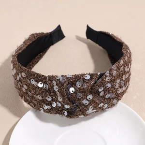 Detail of brown sequined tweed headband with twist knot design on a white ceramic plate