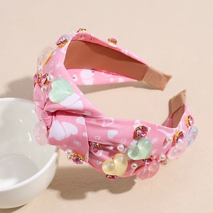 Dettaglio del cerchietto imbottito rosa con cuori bianchi, perle finte e strass lucidi