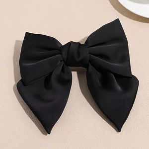 Detail shot of the large black satin bow hair clip on a minimalist textured surface