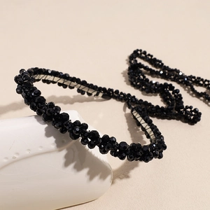Close-up of black beaded headband with faceted crystals on a white ceramic display