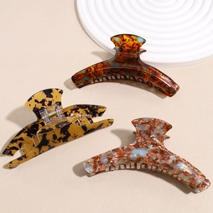 Set of large French tortoiseshell acetate hair claws with gold logo on a beige background