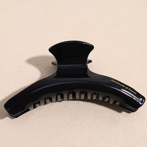 Detail of black glossy hair claw with golden handmade to France logo and curved design