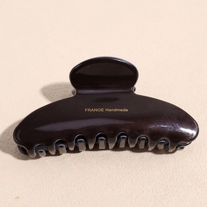 Detailed macro view of smooth dark brown acetate hair claw clip with gold logo