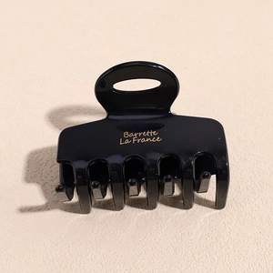 Detail of black glossy hair claw clip featuring gold Barrette La France text and comb teeth