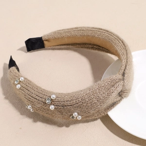 Detail eines khakifarbenen Strickstirnbands mit Perlen und Strass auf einem Teller