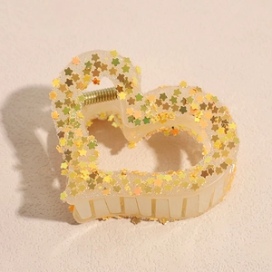 Detail of heart-shaped hair claw clip in cream plastic with golden star sequins