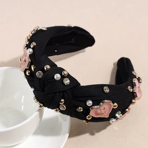 Détail du serre-tête noué noir avec strass, perles et cœurs en émail rose brillant