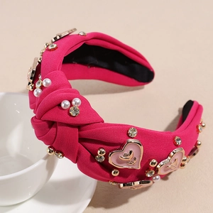 Détail d'un serre-tête noué rose fuchsia avec perles, cristaux et breloques en cœur