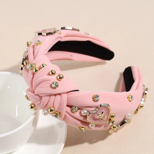 Détail d'un serre-tête torsadé rose avec perles dorées, strass et breloques cœur