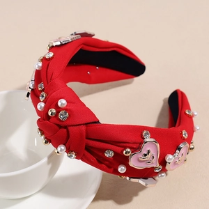 Détail d'un bandeau noué rouge avec perles, strass et breloques en cœur gravées de roses