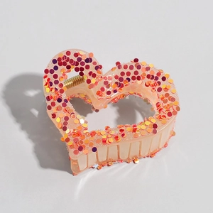 Detail view of heart-shaped claw clip with colorful sequins and golden metal spring