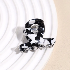 Detail of a mini black and white marble pattern hair claw clip on a white round display