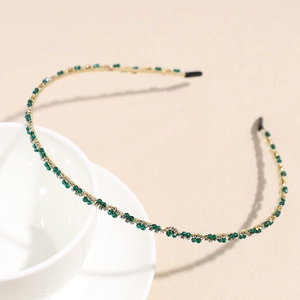 Close-up of thin gold headband with green and white crystals on a white ceramic cup