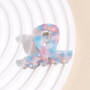 Detail view of pink and blue marbled acetate hair claw clip on a white textured plate
