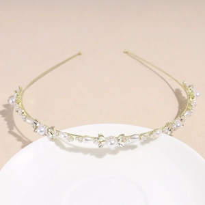 Détail d'un serre-tête doré avec perles et strass sur une assiette en céramique blanche