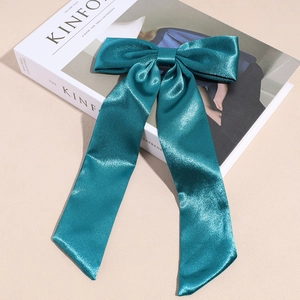 Dettaglio del fermaglio a fiocco in raso verde scuro con nastri lunghi su sfondo bianco