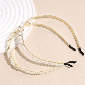 Elegant gold metal headband set with pearls and rhinestones on a beige surface