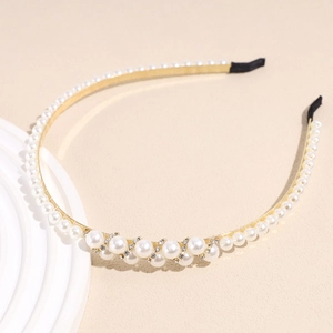 Detailed close-up of a gold metal headband with white pearls and sparkling rhinestones
