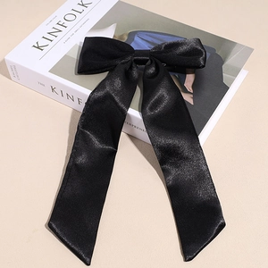 Dettaglio di un grande fiocco per capelli in raso nero con nastri su un libro minimalista