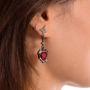 Dettaglio di orecchini a cuore gotici con pietre rosse su modella con design lungo a goccia