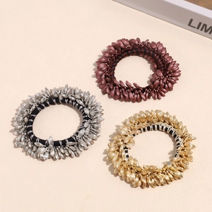 Three wheat-ear elastic hair ties in gold, silver, and bronze on a textured background