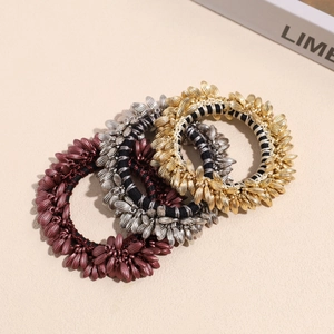 Three-piece wheat ear hair ties set in gold, silver and brown finishes on a textured background