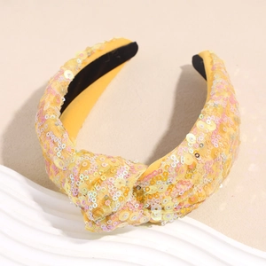 Dettaglio di un cerchietto giallo con paillettes, design a nodo e finitura scintillante