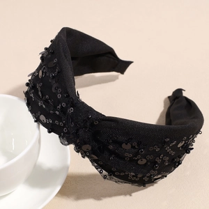 Dettaglio di un cerchietto in rete nera con paillettes lucide e design a nodo