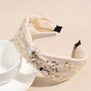 Dettaglio della fascia beige con nodo, paillettes dorate e perle finte bianche