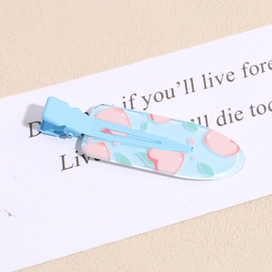 Close-up of a blue duckbill hair clip with peach patterns on a decorative white card