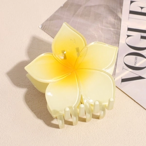 Detailed macro view of a glossy yellow plumeria flower hair claw clip on a stylish magazine