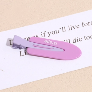 Close-up of pink and purple matte duckbill hair clip with Grape text on a beige surface