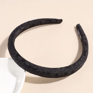 Dettaglio di un cerchietto nero spesso con trama floreale a rilievo e finitura satinata