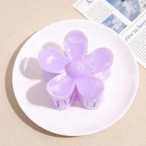 Detail view of a translucent purple flower hair claw clip on a white ceramic plate