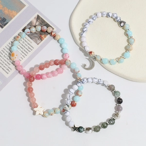 Three handmade crystal bead bracelets with moon and star charms on a ceramic tray