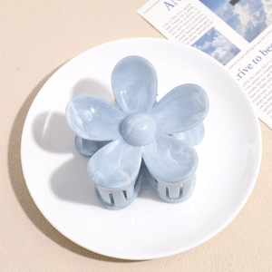 Close-up of a blue marble flower hair claw clip on a white decorative ceramic plate