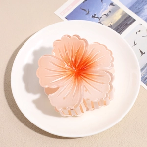 Close-up of a pink gradient hibiscus flower hair claw clip on a white ceramic plate